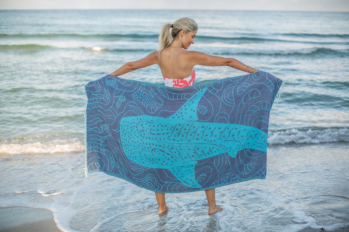 Woman holding a blue towel with whale design on a beach