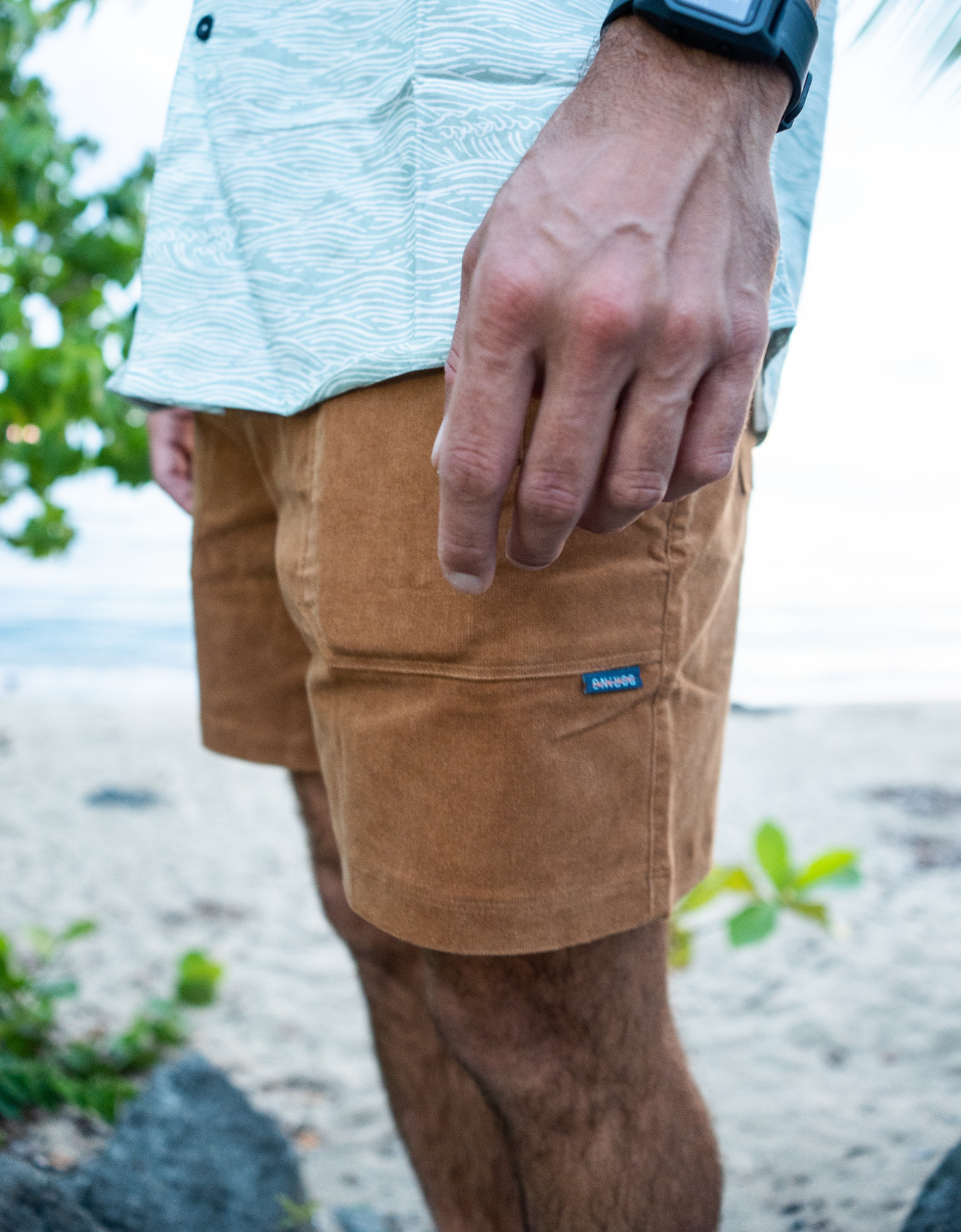 Person wearing brown shorts with a visible brand logo on a beach.