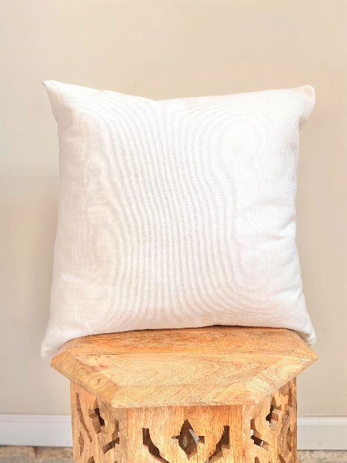 White pillow on a wooden stool against a beige wall