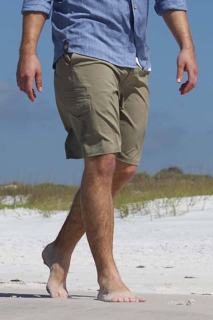 Person wearing green shorts and a blue shirt walking on a sandy beach.