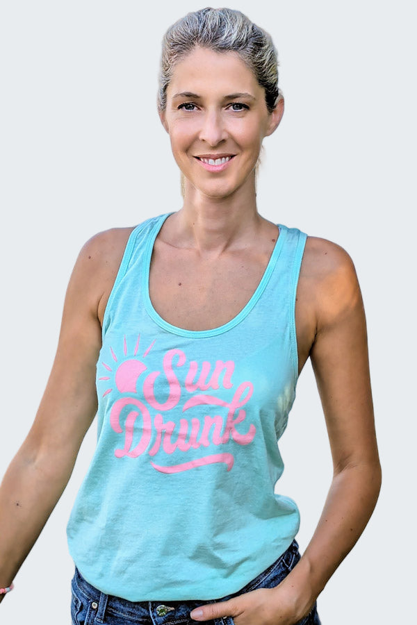 Woman wearing a light blue tank top with 'Sun Drunk' text by a body of water.