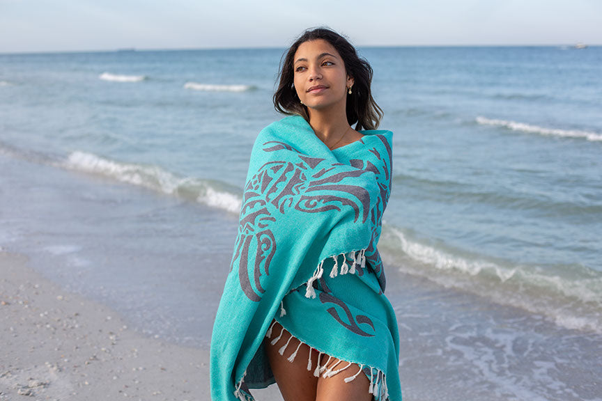 Woman wrapped in a teal towel with a pattern on a beach