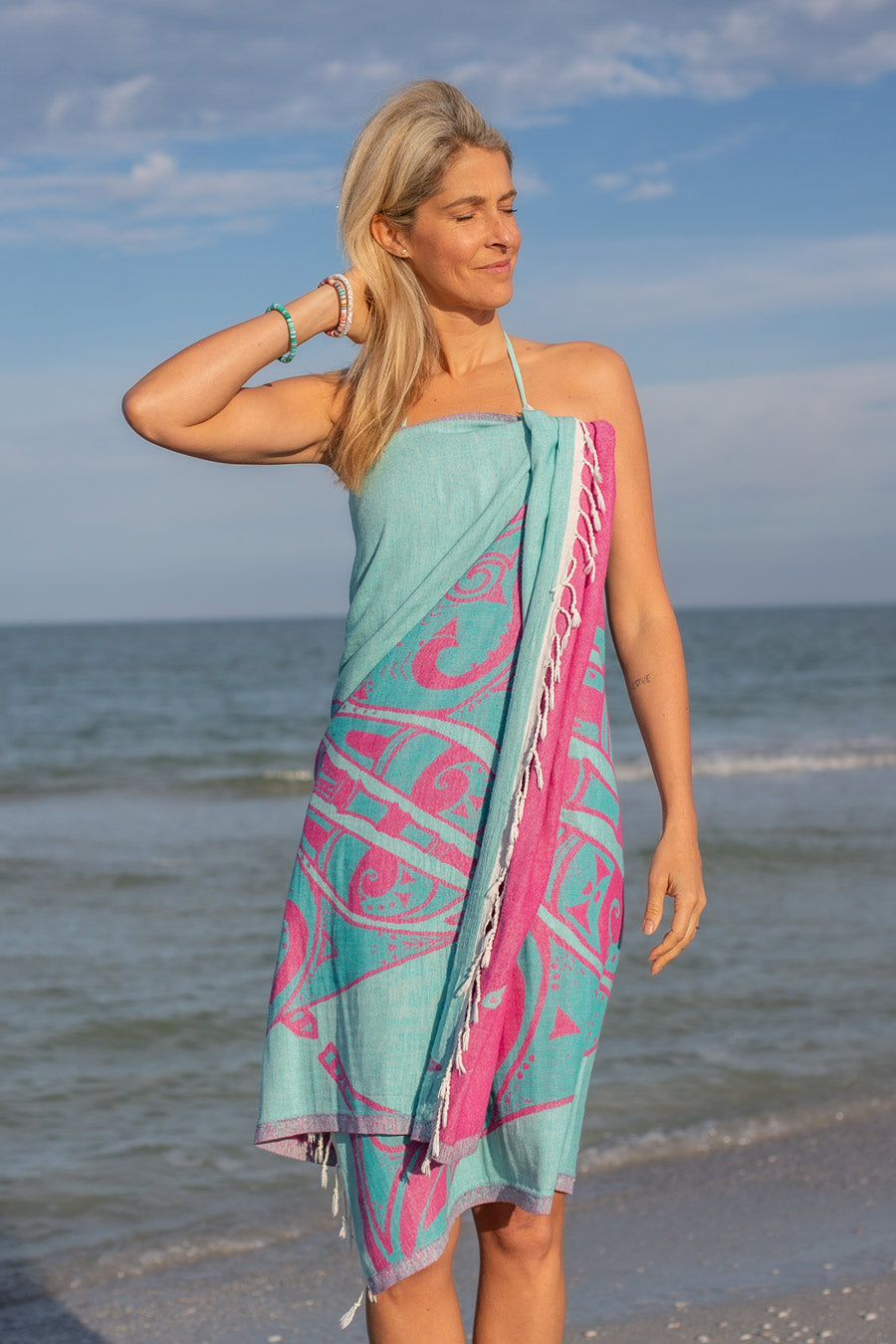 Woman on a beach wearing a turquoise and pink patterned towel.