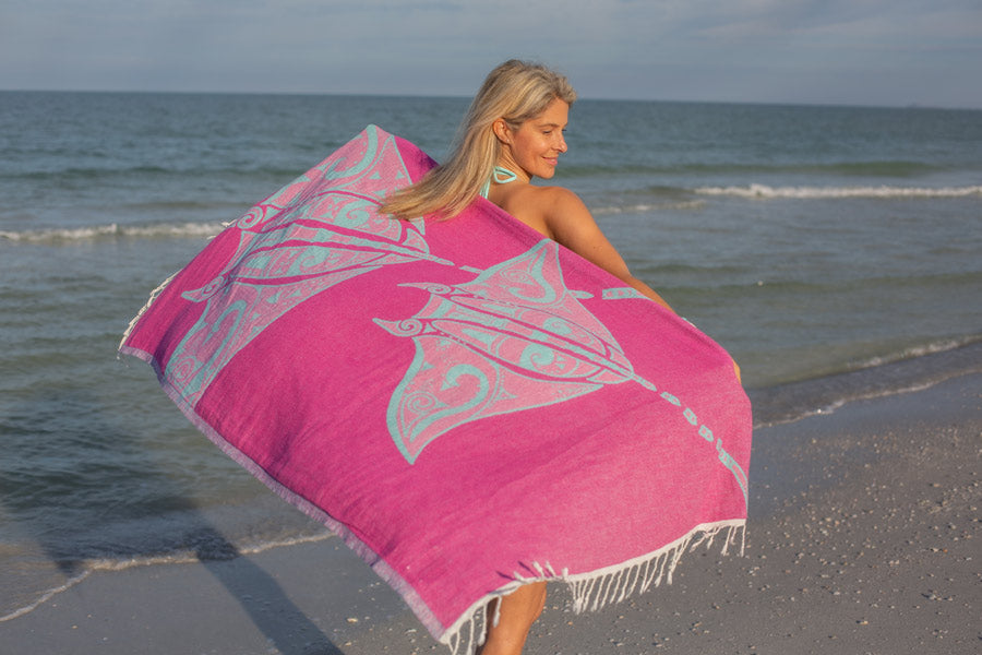 Woman holding a pink and white patterned towel on a beach