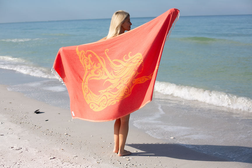 Person holding a red towel with a dragon design on a beach