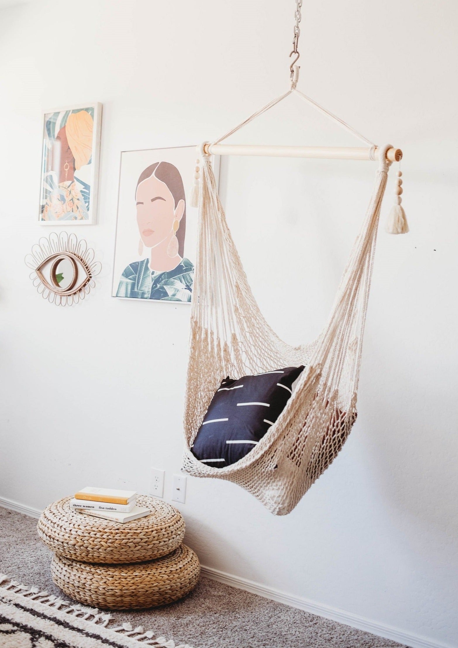 Hanging chair with a pillow in a room with wall art and a footstool.
