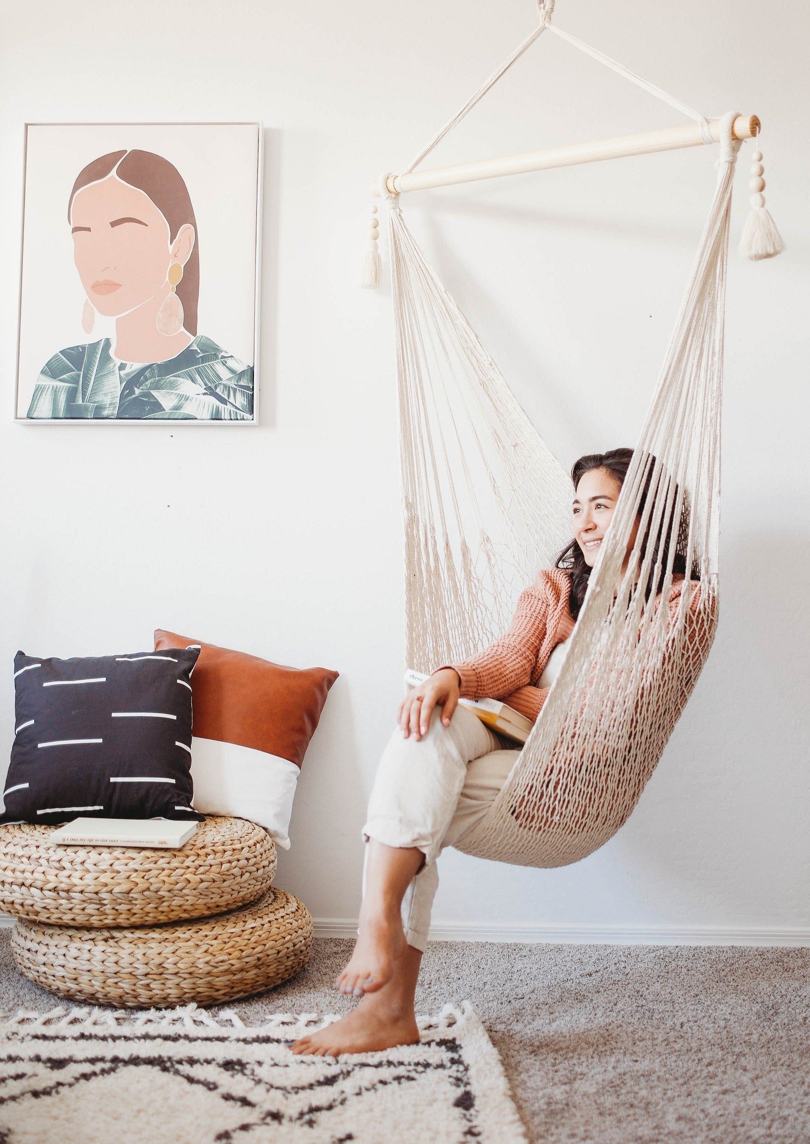 Woman sitting in a woven chair in a cozy room with a framed portrait on the wall.