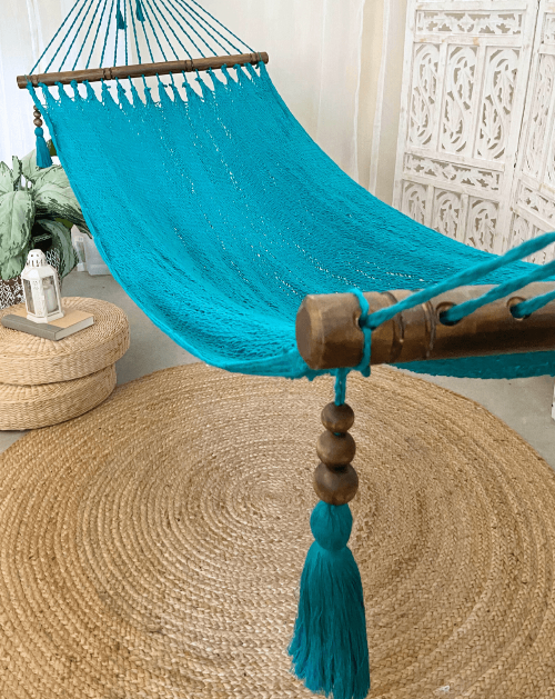Turquoise hammock with wooden beads and tassels on a woven floor mat.