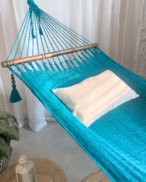 Turquoise hammock with a white pillow against a neutral background