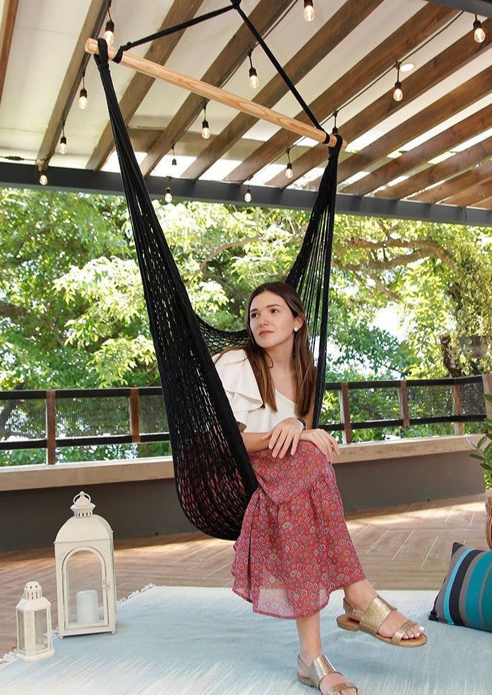 Woman sitting in a black hammock on a wooden deck with greenery in the background