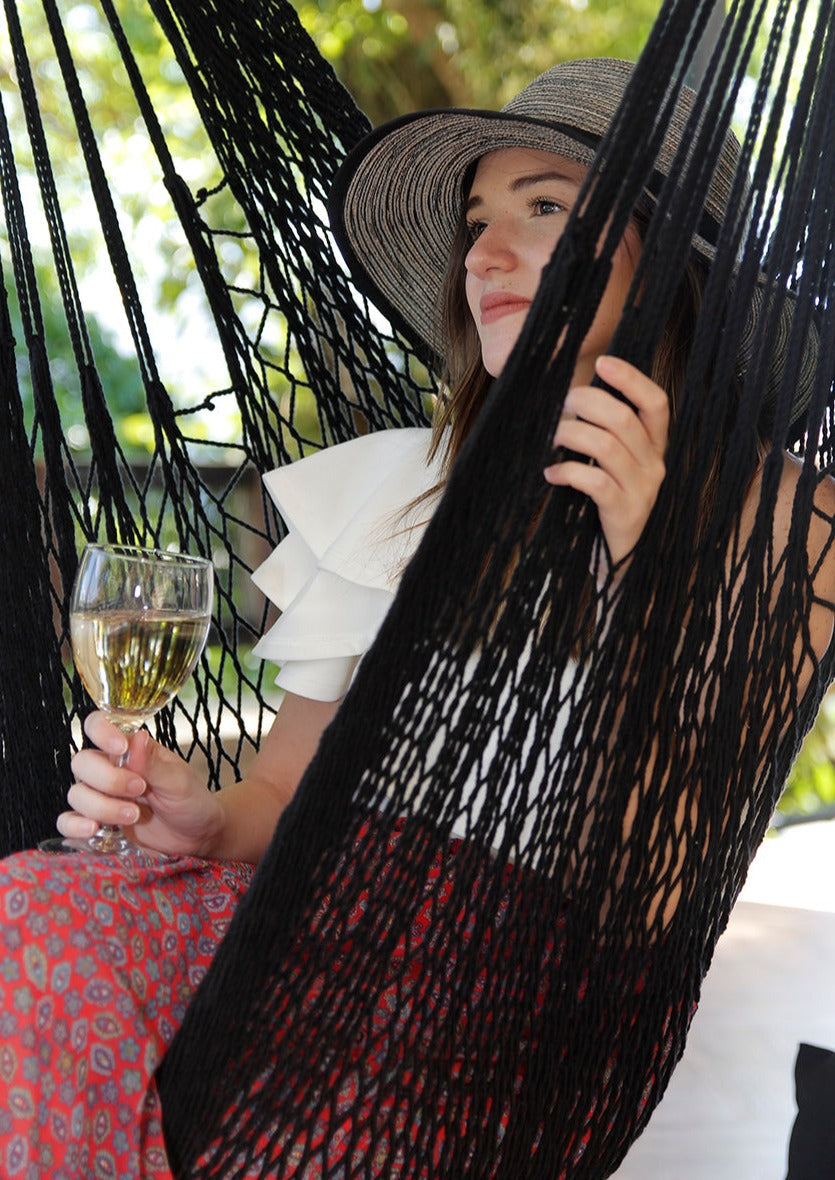 Woman in a hammock holding a glass of wine, wearing a wide-brimmed hat.