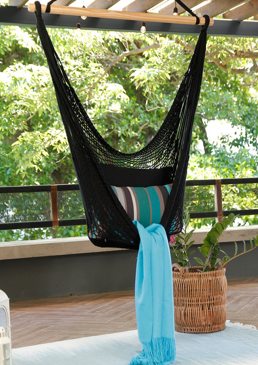 Black hammock with striped cushion and blue towel on a wooden deck with greenery in the background