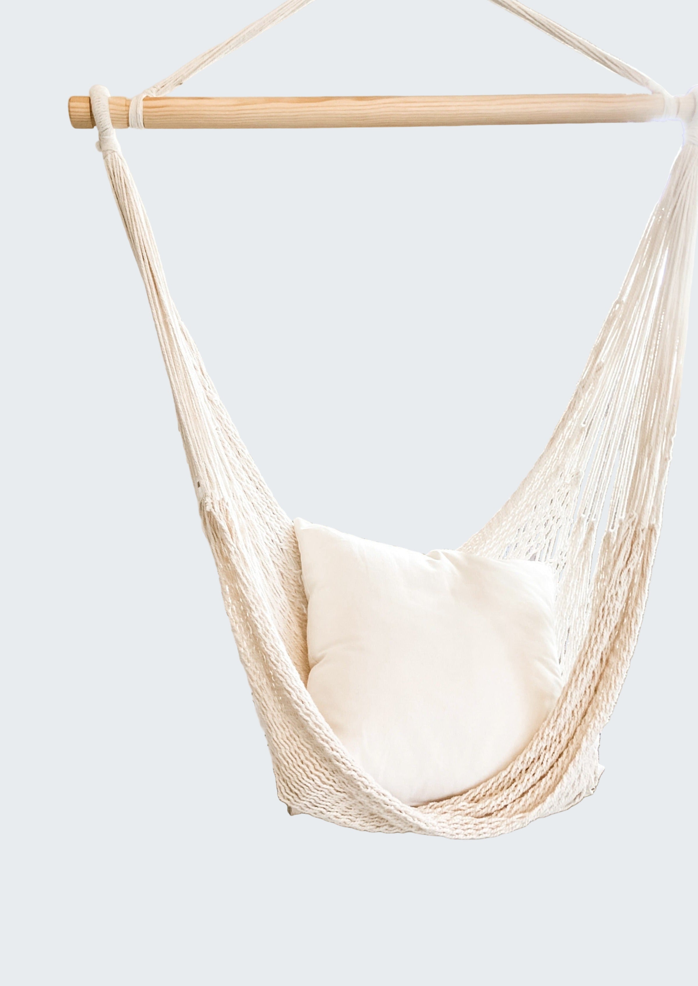 Beige hammock chair with a white pillow in a room with decorative screen and plant.