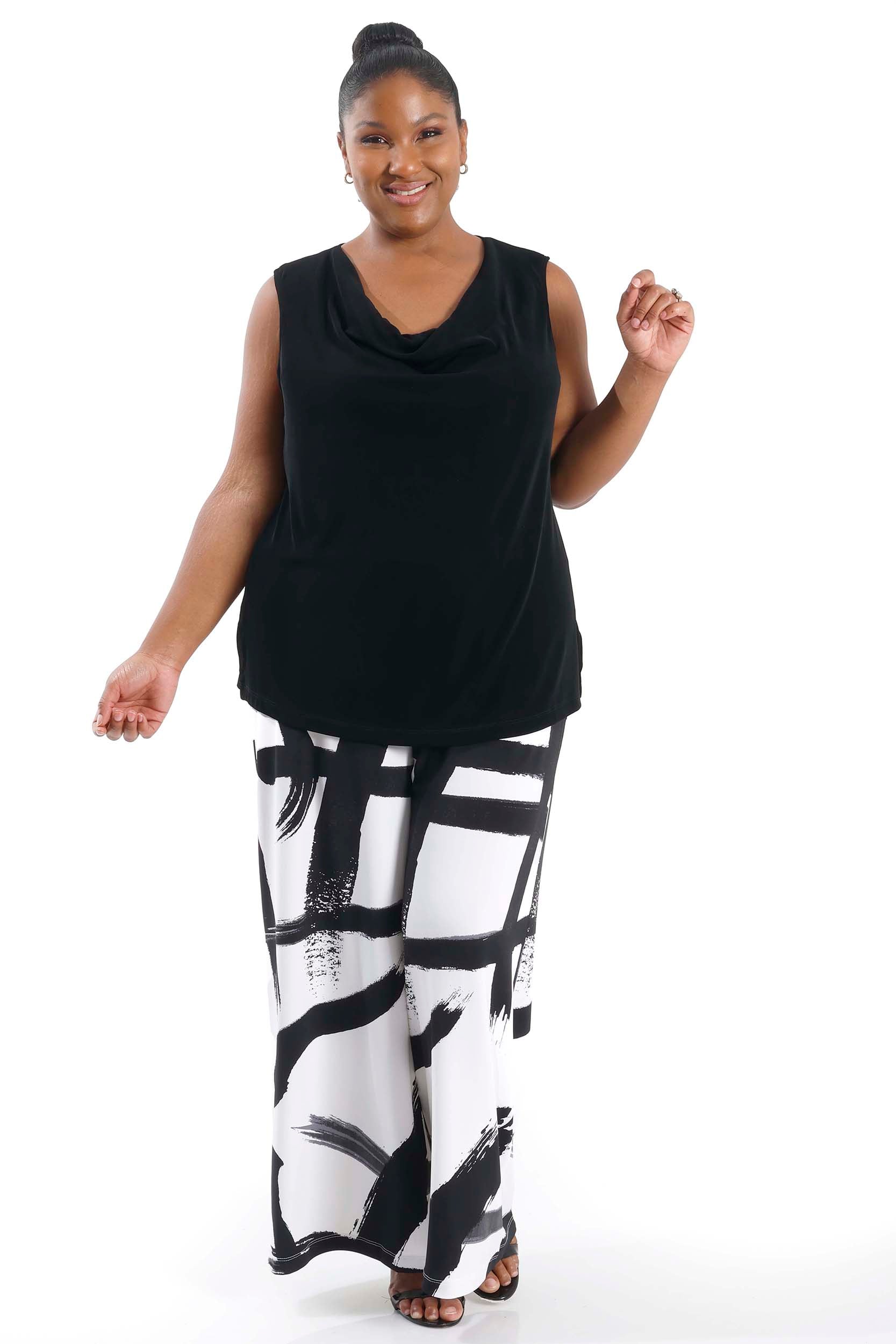 Woman wearing a black sleeveless top and white pants with black abstract patterns on a white background