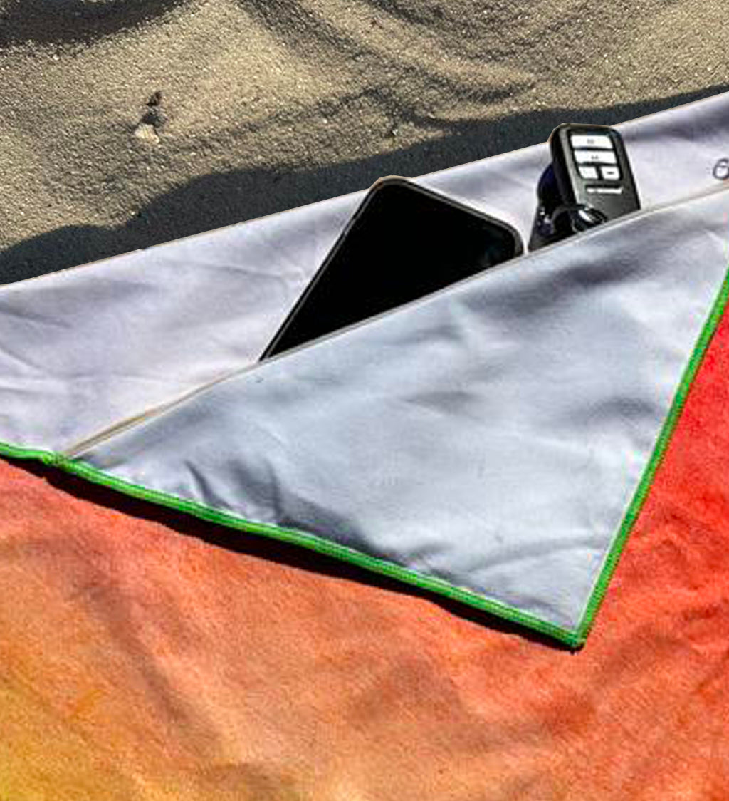 Colorful towel with a phone and remote control on a sandy surface